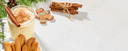 Christmas banner with eggnog with cinnamon and ginger cookies on white wooden backdrop.