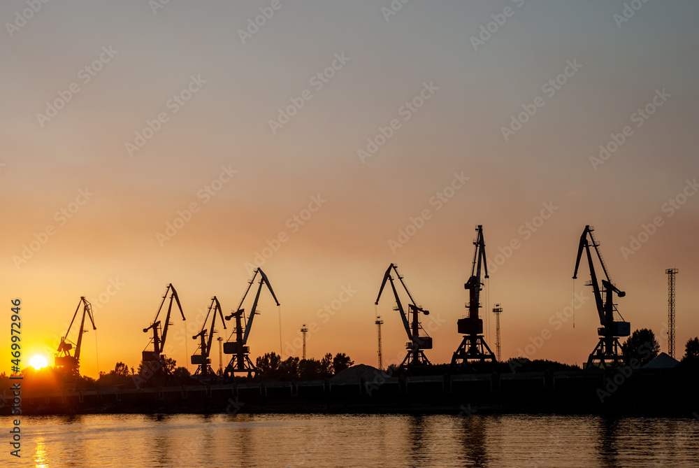 Silhouettes of tower cranes against the background of a sunset red sky.