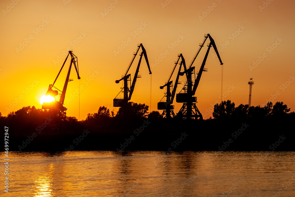 Silhouettes of tower cranes against the background of a sunset red sky.