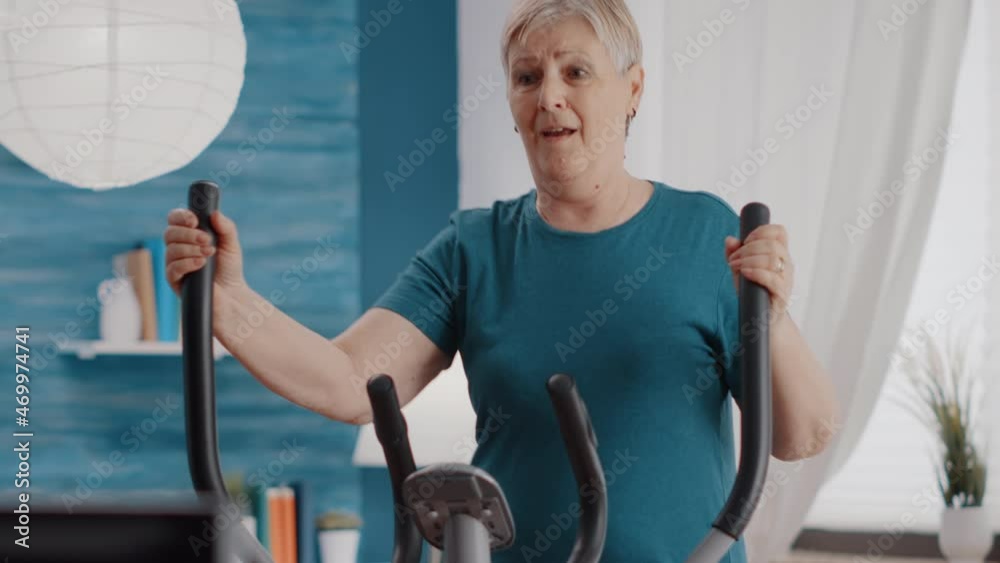 Close up of retired woman riding stationary bicycle at home. Senior person using cardio machine to cycle and do physical exercise on static bike. Pensioner cycling and doing fitness activity