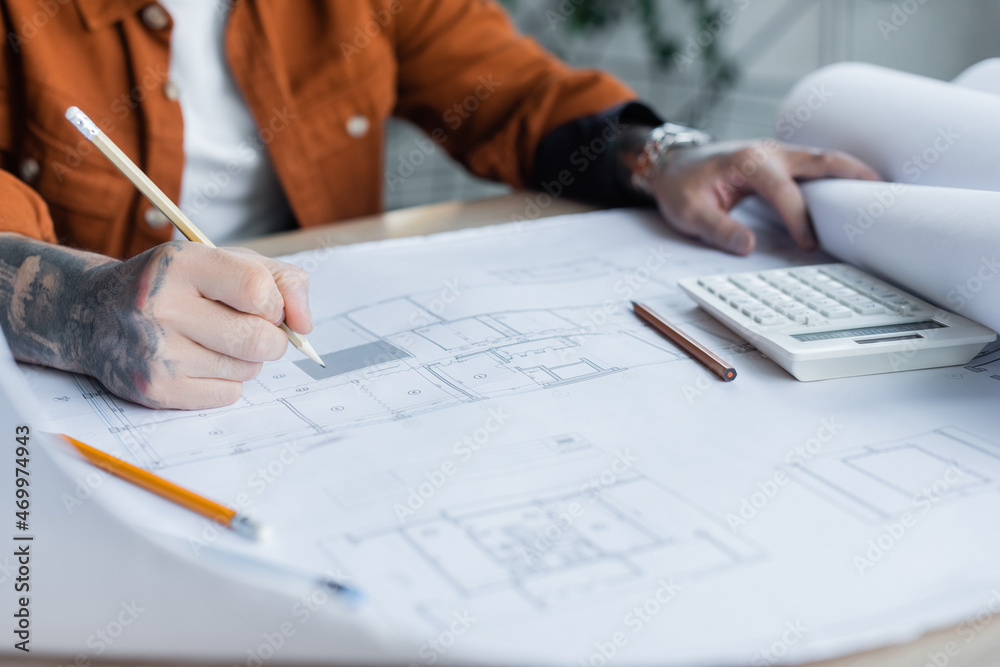 cropped view of tattooed engineer drawing architectural plan near calculator on desk cropped view of tattooed engineer drawing architectural plan near calculator on desk
