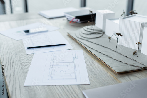 house models and blueprints near blurred notebooks and smartphone on wooden desk