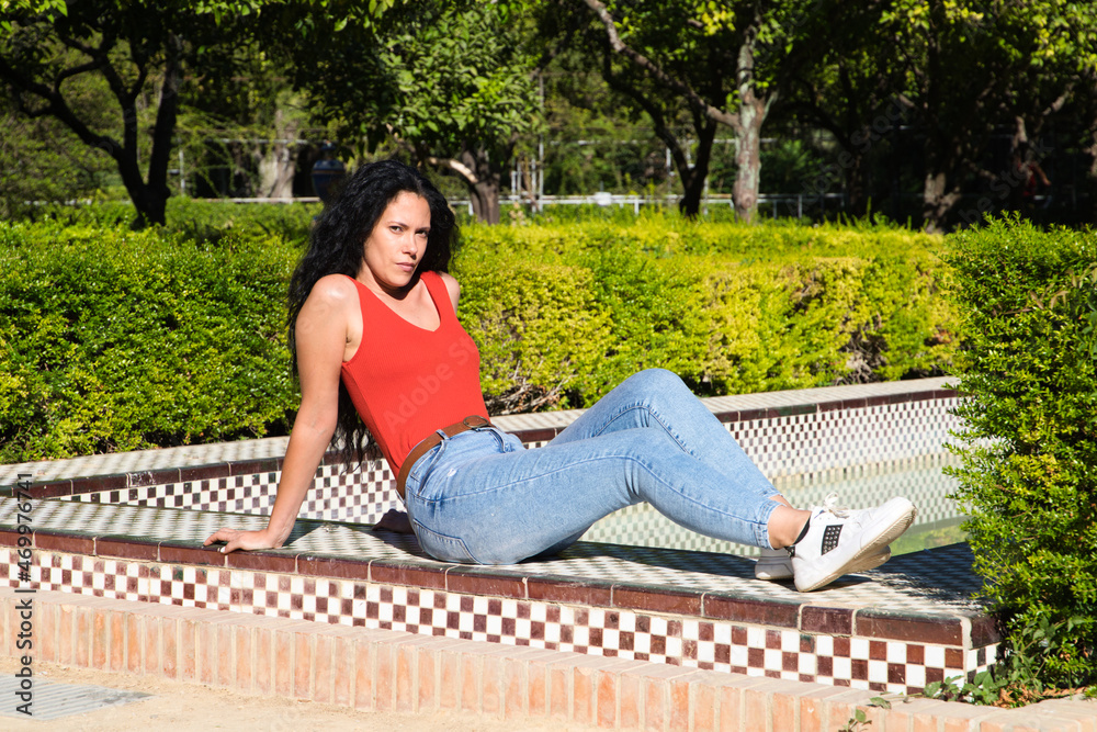 a beautiful, adult, dark-haired, curly-haired woman with Latin features is sunbathing on a tiled bench in the park. Four seasons concept a beautiful, adult, dark-haired, curly-haired woman with Latin features is sunbathing on a tiled bench in the park. Four seasons concept