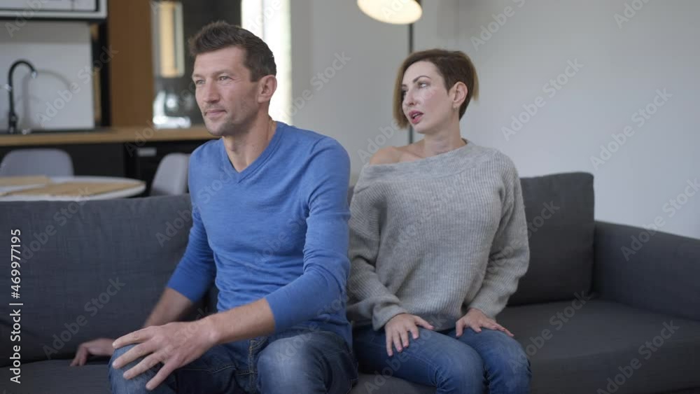 Irritated unloving husband turning from wife touching shoulder of spouse. Portrait of upset Caucasian man sitting on couch in living room with woman at background sitting down sighing Irritated unloving husband turning from wife touching shoulder of spouse. Portrait of upset Caucasian man sitting on couch in living room with woman at background sitting down sighing