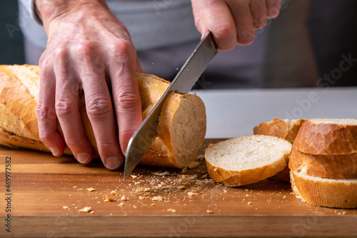 hands cutting a freshly baked baguette into slices on a wooden board, front view