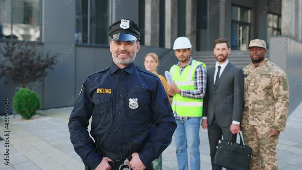Waist up portrait view of the policeman posing with people of different occupations standing at the street at the background. Jobs concept Waist up portrait view of the policeman posing with people of different occupations standing at the street at the background. Jobs concept