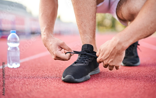 Close-up of sportsman tying sneakers - Unrecognizable man stopping lacing shoe outdoors - Athletic shoes concept - A plastic bottle of mineral water in the background