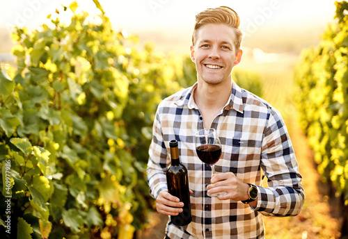 Принти на полотні Portrait of a young, millennial vintner holding a glass and a bottle of organic