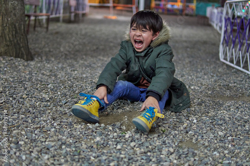 Foto sad and upset child latin boy shouting and crying sitting on the pebble floor in a amusement park