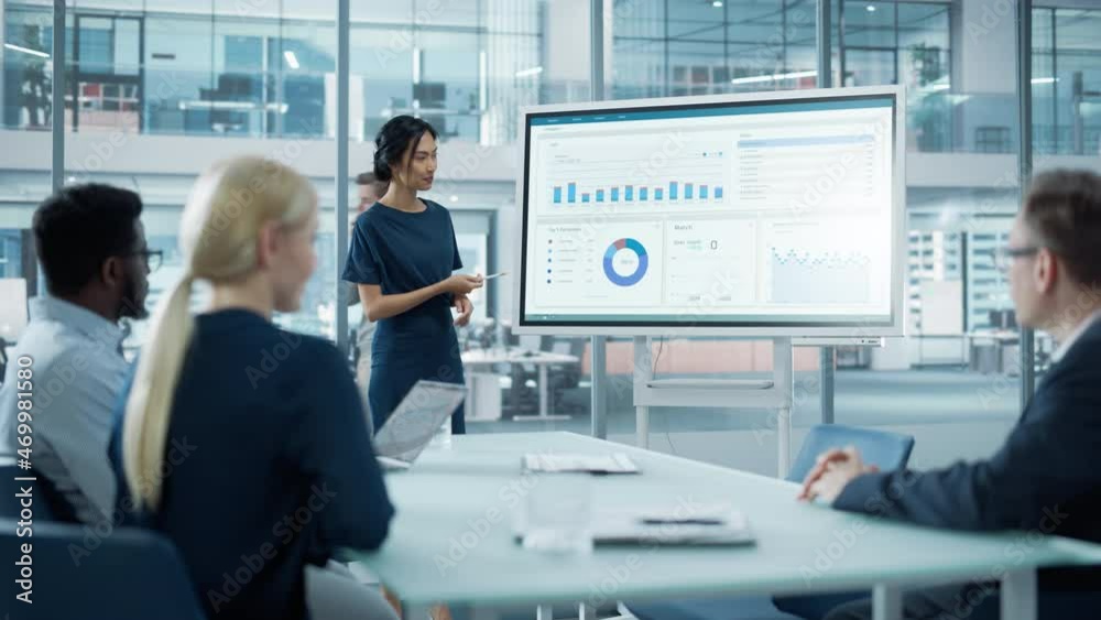 Female Operations Manager Holds Meeting Presentation for a Team of Economists. Asian Woman Uses Digital Whiteboard with Growth Analysis, Charts, Statistics and Data. People Work in Business Office. Female Operations Manager Holds Meeting Presentation for a Team of Economists. Asian Woman Uses Digital Whiteboard with Growth Analysis, Charts, Statistics and Data. People Work in Business Office.