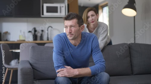 Handsome unloving husband moving away from wife trying hug spouse. Portrait of sad frustrated Caucasian man argued with woman sitting on couch in living room. Lifestyle and relationship problems photo