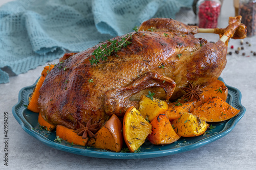 Roasted whole duck served on a plate with fresh thyme and orange-roasted pumpkin. Dish for festive dinner. Close up, selective focus.