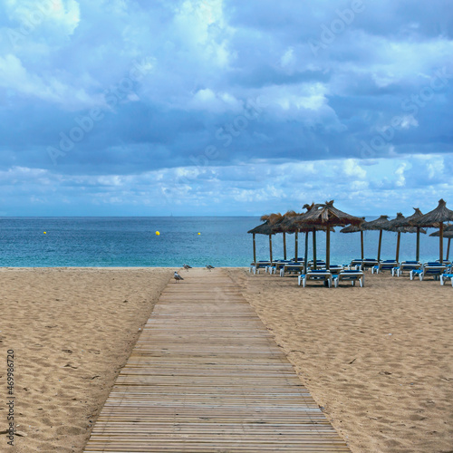 wooden walkway on a sandy beach against the backdrop of the sea  straw umbrellas and plastic sunbeds