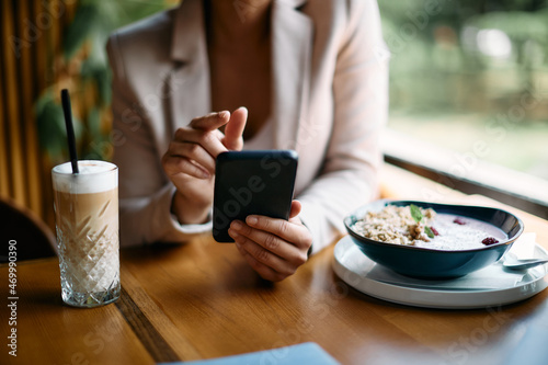 Close-up of businesswoman uses smartphone during her breakfast in cafe.