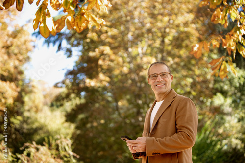 man with jacket and cell phone in hand outdoors smiling looking to the side mature couple taking a selfie on location