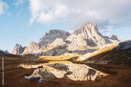 Clear water of alpine lake Piani in the Tre Cime Di Laveredo National Park, Dolomites, Italy. Picturesque landscape with Schusterplatte mountains, orange grass and small lake in autumn Dolomite Alps
