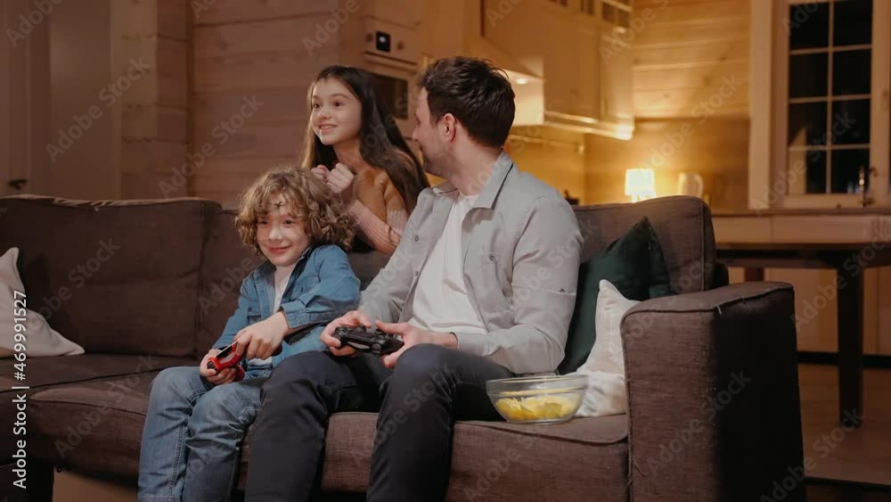 Father playing with his son in game console and losing, laughing sitting on sofa. Son wins against his father at the game console. Family spends time together in lockdown. 50fps. High quality 4k 