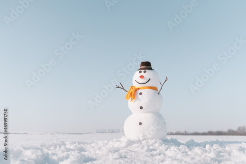 Fototapeta Funny snowman in stylish brown hat and yellow scalf on snowy field