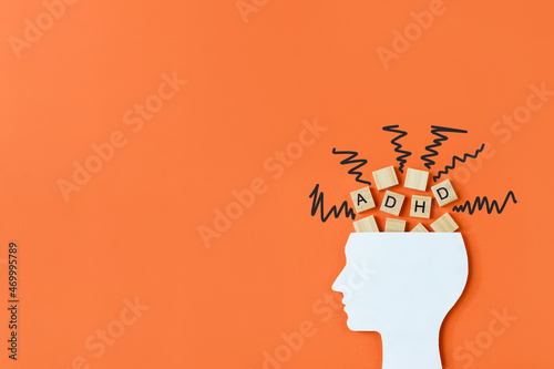 Silhouette of human head with chaotic lines and wooden blocks with the letters ADHD on orange background. Minimal concept of attention deficit hyperactivity syndrome. Copy space photo