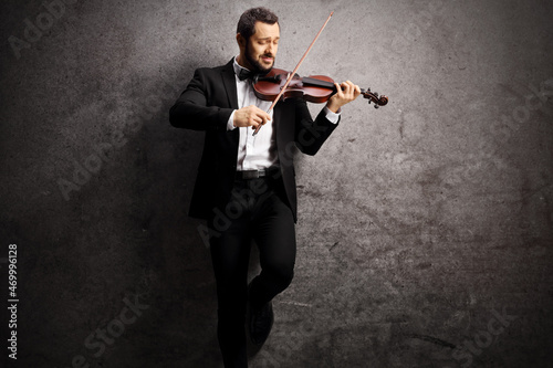 Elegant young man playing a violin and leaning on a gray rugged background