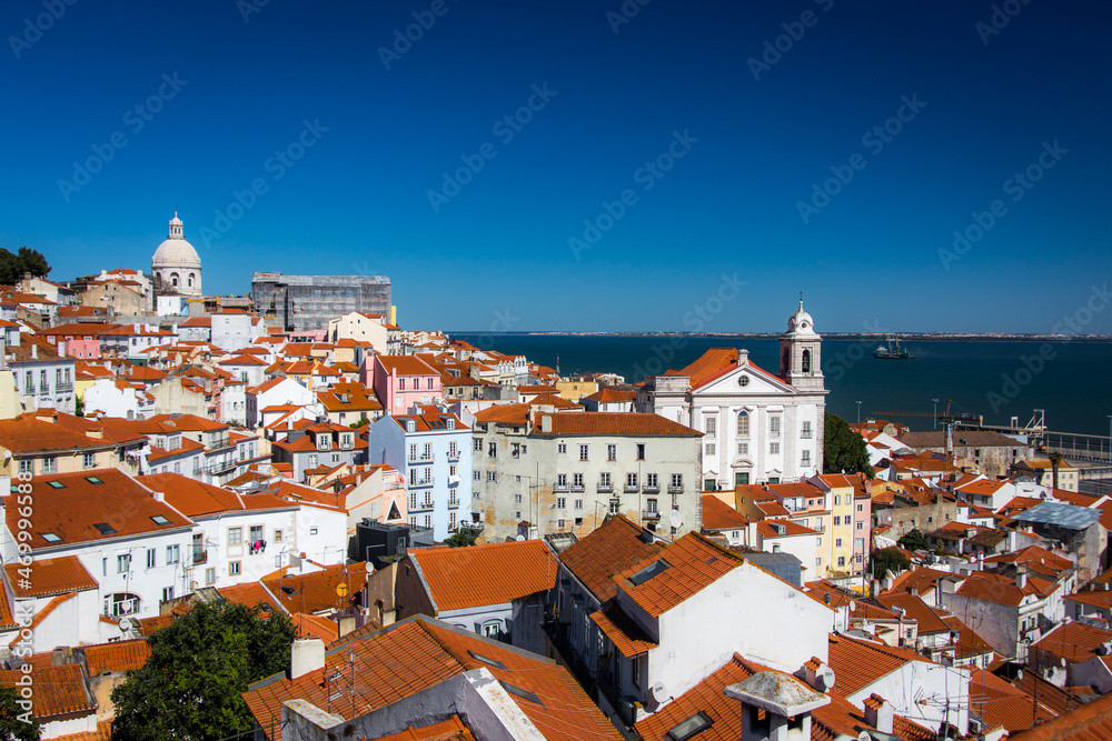 Beautiful city skyline of Lisbon with red brick roofs, clear blue sky and historical buildings from the Alfama District.