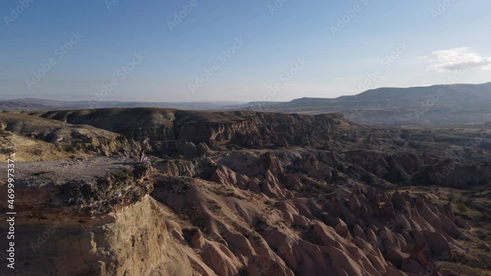 Woman Sitting on the Cliff and Enjoys the View of Specific Mountains in Cappadocia, Turkey Woman Sitting on the Cliff and Enjoys the View of Specific Mountains in Cappadocia, Turkey
