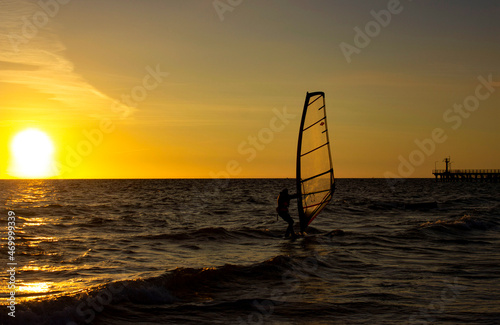 Sap board with a sail on the background of an orange sunset. Sea with waves. Surfer silhouette. Marine sports.