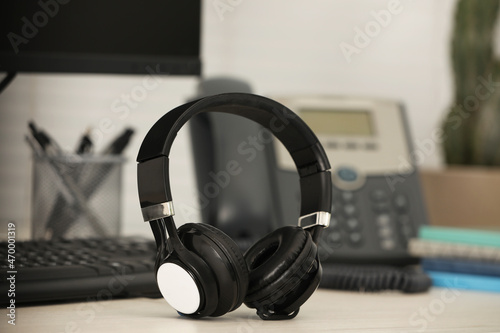 Modern headphones, desktop telephone and computer on table indoors © New Africa