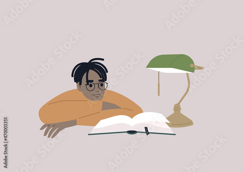 A young male African character leaning on arms and reading a book, educational process, a university student preparing for the exams in the library