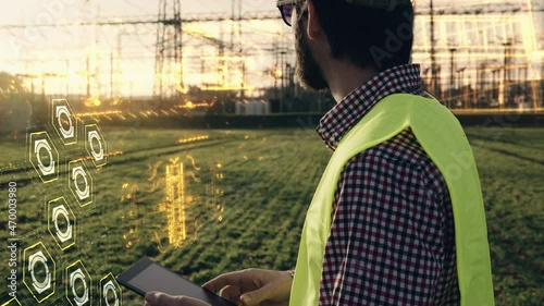 Electric engineer wearing helmet safety vest working with tablet near high voltage lines power station holographic energy animation during sunset shot in 4k super slow motion