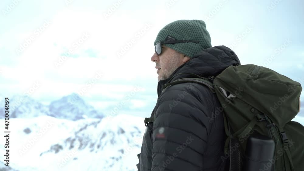 Man in warm jacket and with backpack looking away in the snowy mountains Man in warm jacket and with backpack looking away in the snowy mountains