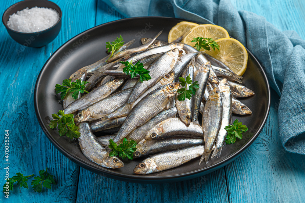 Salted sprat with lemon in a plate on a blue background. Salted sprat with lemon in a plate on a blue background.