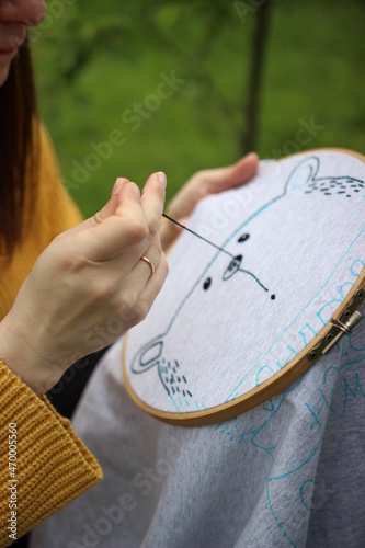 The process of hand embroidery. Female holds a needle in her hands and embroiders a pattern with black threads on a grey cloth
