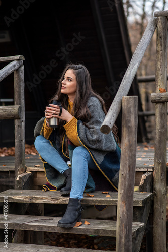 The girl enjoys the smell of coffee and autumn colors in front of the mountain house