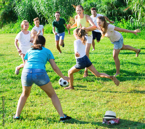 Cheerful positive smiling parents with children gaily spending time together playing with ball outdoors © JackF