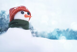 Little cute snowman in a knitted orange hat and a green scarf with a carrot nose in a snowy field close-up, copy space. Christmas background with winter symbol