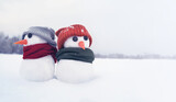 Two little cute snowmen in hats and scarves in a snowy field close-up. Christmas background with symbols of winter