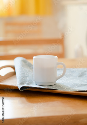 White coffee mug with napkin on table in real kitchen interior with bright natural sunlight