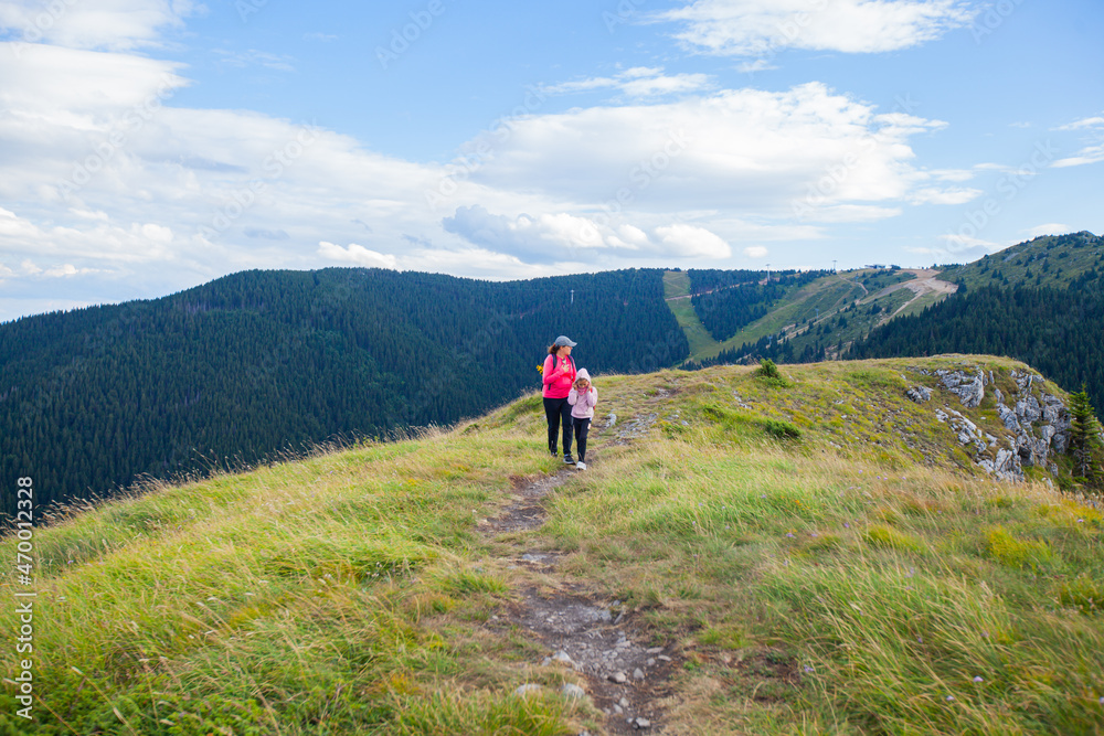 Mother and daughter hiking on mountains at beautiful summer day.