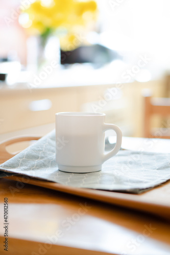 White coffee mug with napkin on table in real kitchen interior with bright natural sunlight