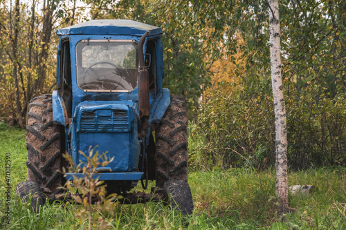 An old blue tractor in a field with tall grass among the trees.