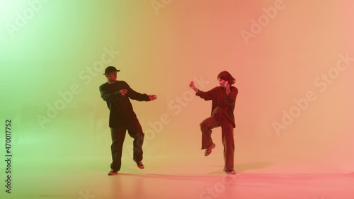 Professional choreographers dancing hip hop on color changing neon background. Man and woman dancers showing movements, pair dance, duet. Modern dance school for teenagers.
