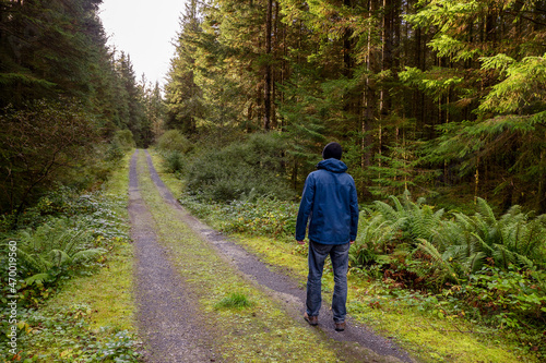 Man walking on a small road in a forest. Fresh air and healthy habit concept. Man dressed in blue jacket and jeans and black hat. Outdoor activity concept.
