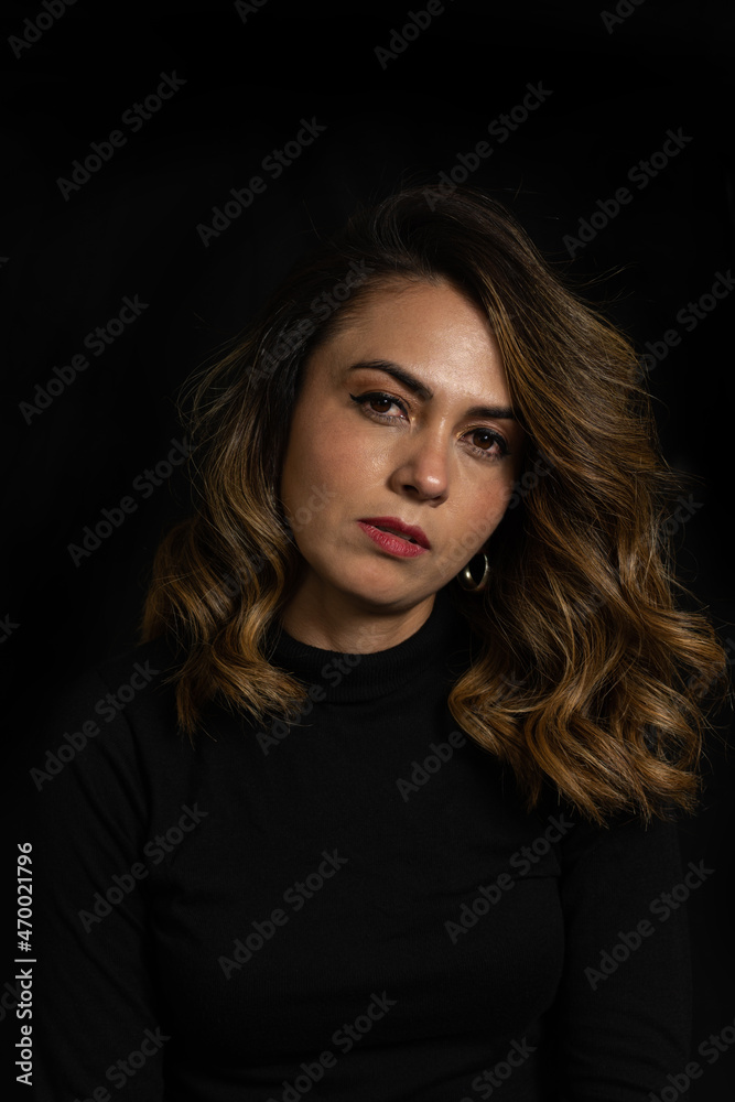 Dramatic portrait of a Latina woman with serious or arrogant expression looking straight into the camera over black background Dramatic portrait of a Latina woman with serious or arrogant expression looking straight into the camera over black background