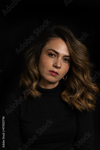 Dramatic portrait of a Latina woman with serious or arrogant expression looking straight into the camera over black background © Julian