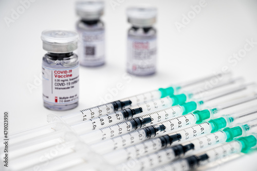 Coronavirus vaccination against SARS-CoV-2. Medical syringes, each with a dose of COVID-19 vaccine, and several glass vials in the background.