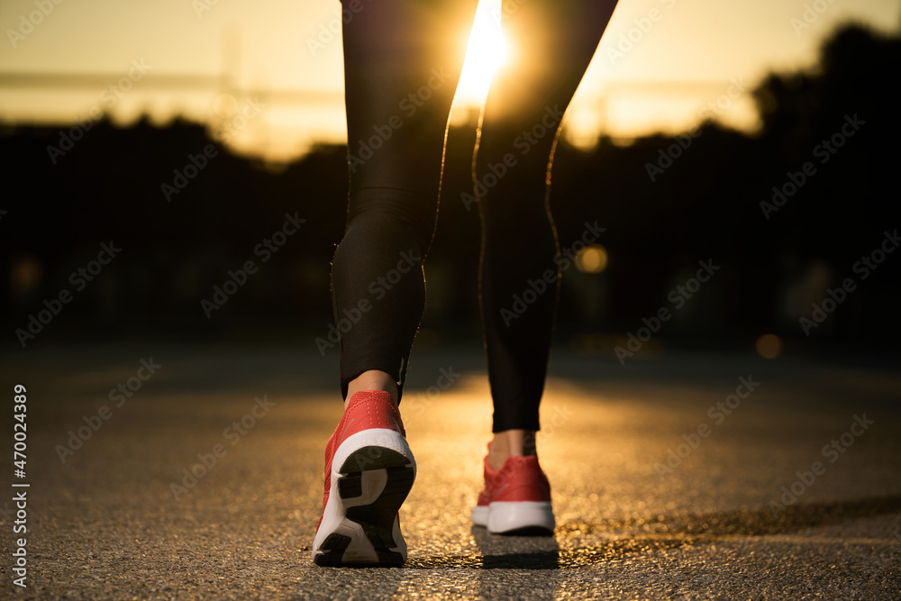 women's legs and feet walking in sneakers on asphalt in sunshine