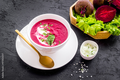 Red beet soup in white bowl with raw beet roots