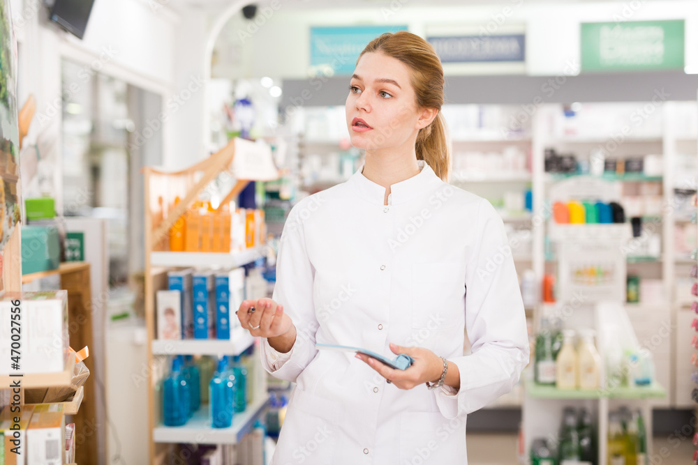 Smiling female pharmacist checking assortment of drugs in pharmacy. High quality photo