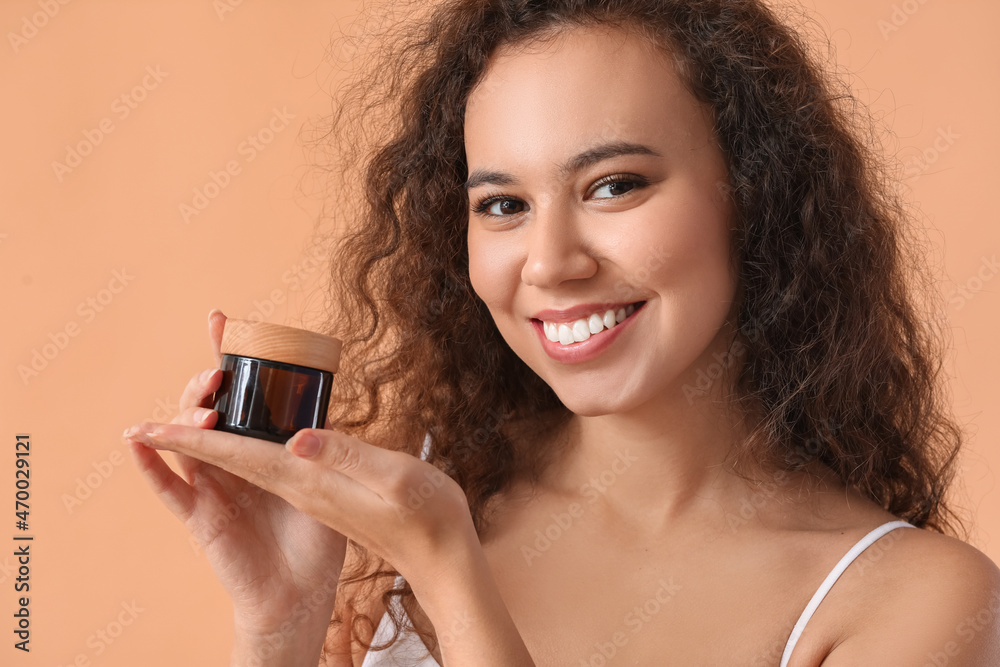Beautiful African-American woman with cream in jar on color background